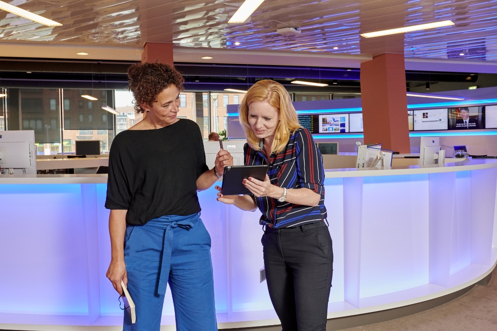 Susan en een collega kijken op een I-pad en staan in de newsroom van het CBS