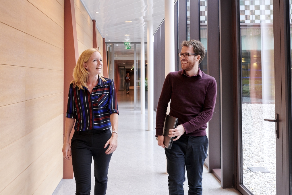 Susan loopt pratend met een collega door de gang