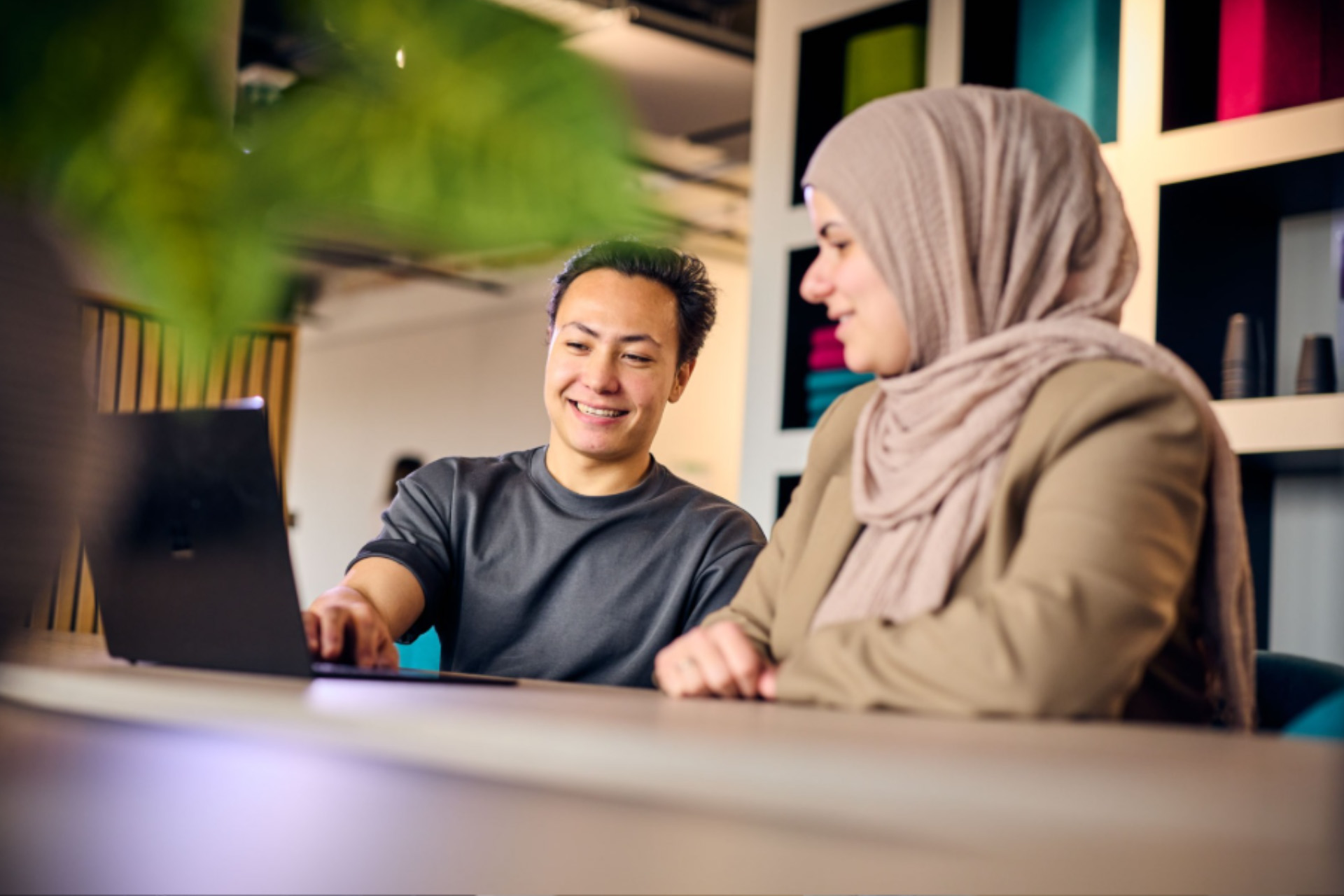 2 collega's van KVK lachend achter laptopscherm, samen aan het werk