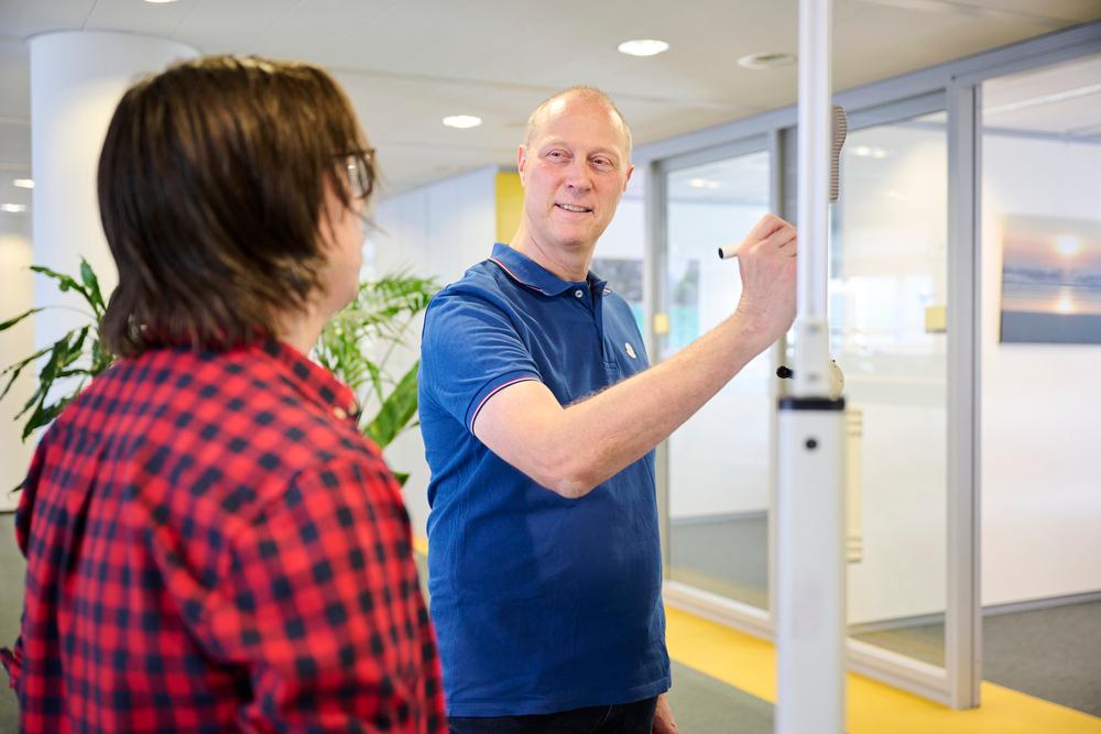Medewerker van Logius schrijft op het bord en kijkt andere collega aan