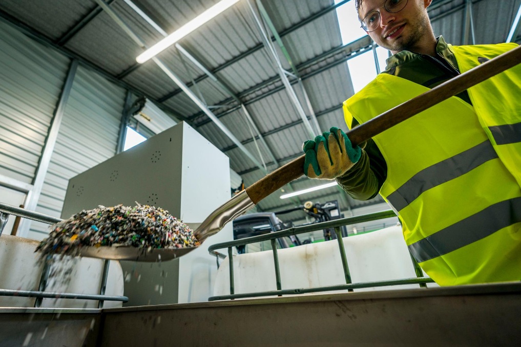 Recycling van plastic in een fabriek. Medewerker schept plastic