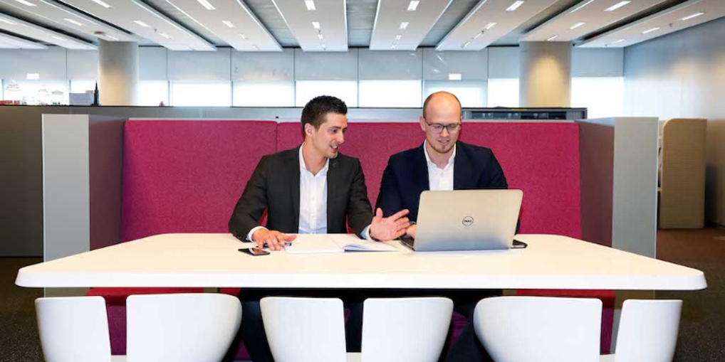 Menno met collega in gesprek achter de laptop op kantoor