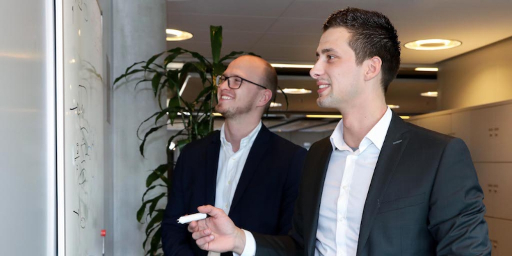Menno en collega bekijken lachend wat ze op het whiteboard hebben geschreven