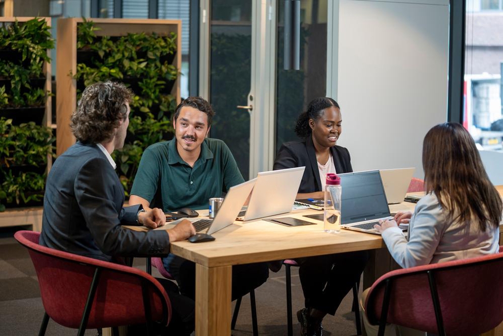 4 collega's met elkaar rond de tafel, met laptops