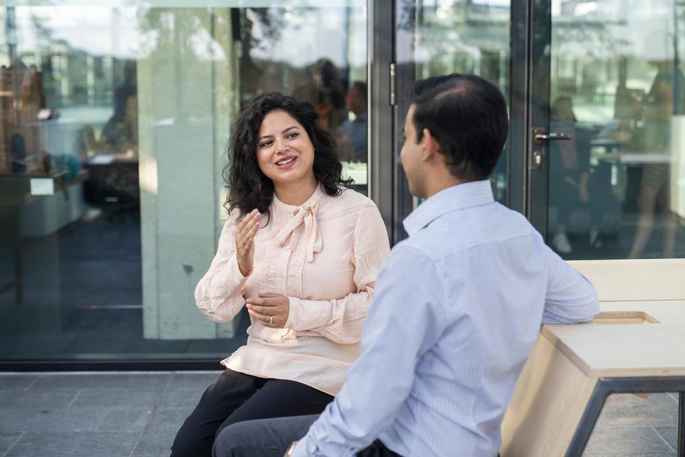 2 collega's met elkaar in gesprek, zitten op een bank buiten