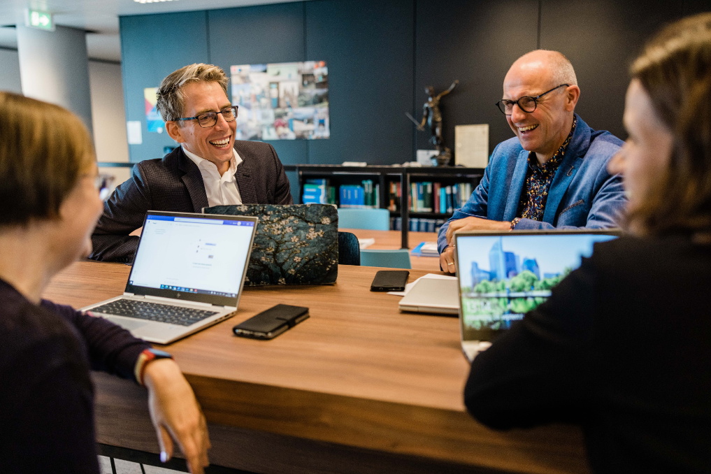 Een groep collega's bij het ministerie van IenW overleggend en lachend aan tafel