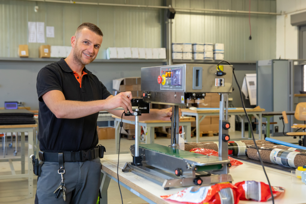 Tommy staat in de werkplaats bij de machine voor het verpakken van zakken hondenbrokken