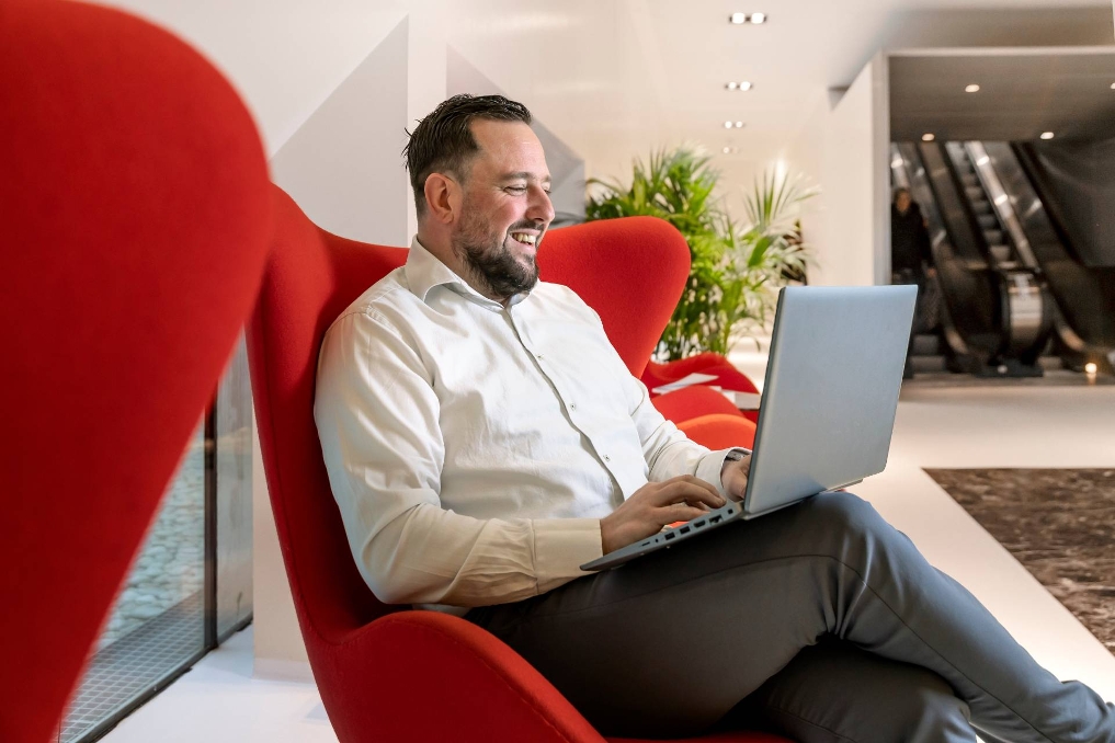 Sam in een rode stoel aan het werk op zijn laptop. Hij is productmanager kwaliteit bij het NFI