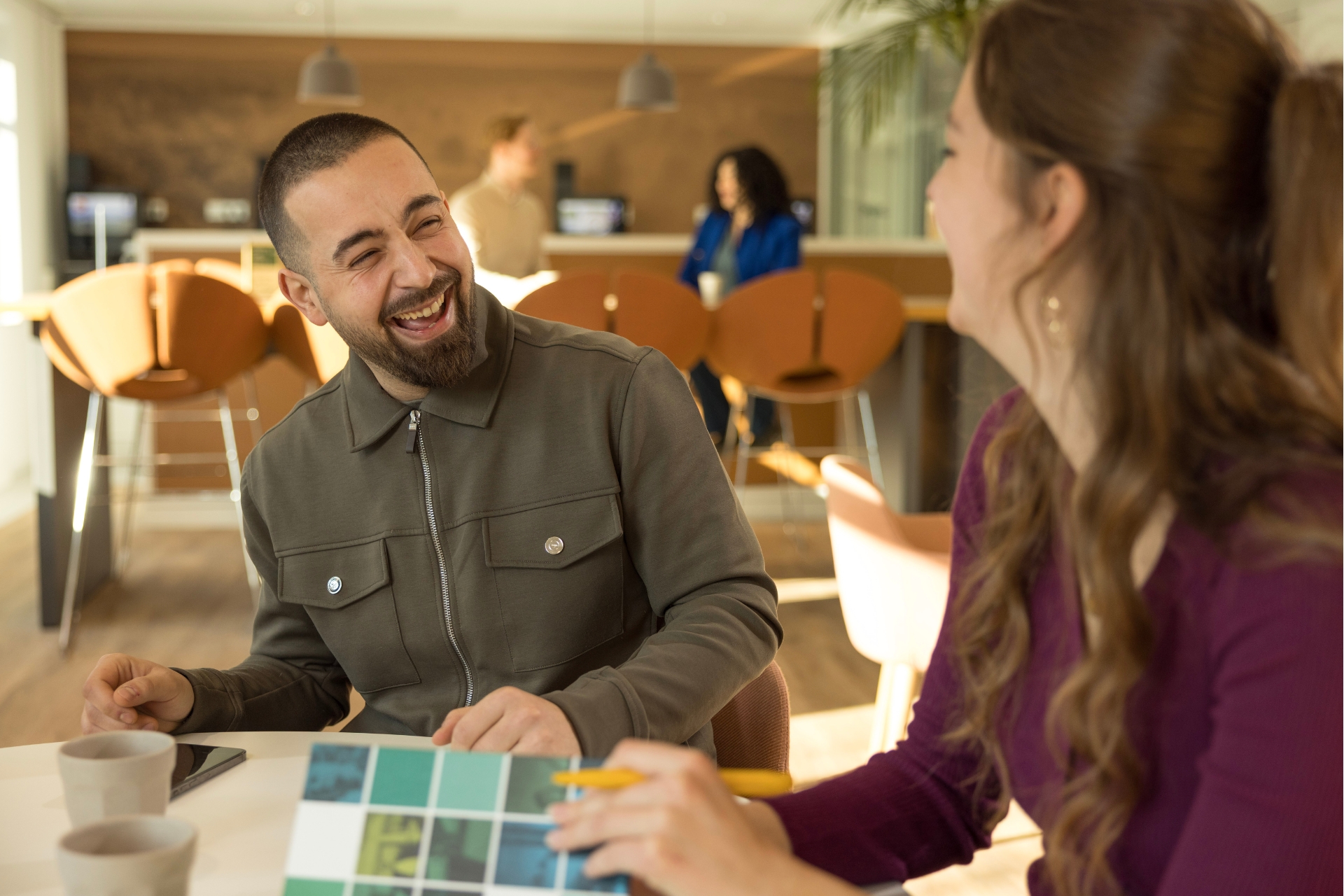 2 collega's van het OM zitten aan tafel en lachen naar elkaar