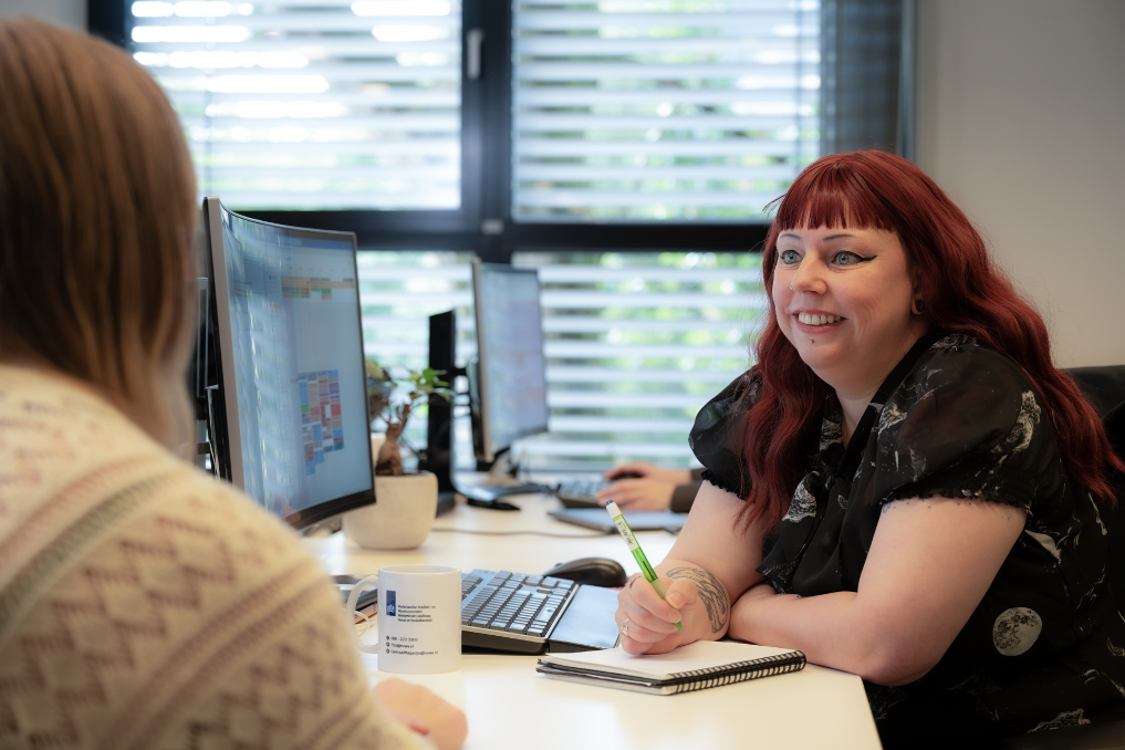 Sylvia met een collega in gesprek achter de laptop. Ze is managementassistent bij de NVWA