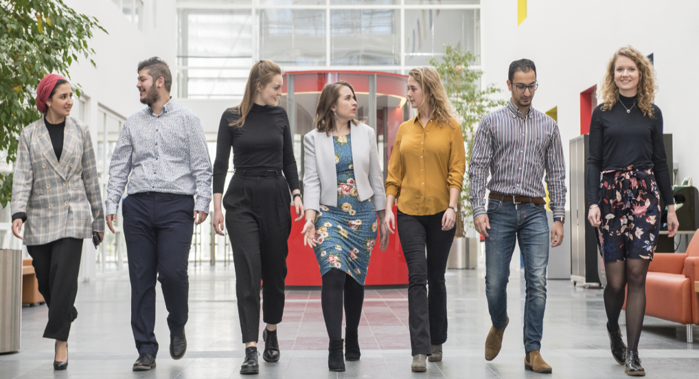 Foto van 7 rijkstrainees op een rij die aan komen lopen