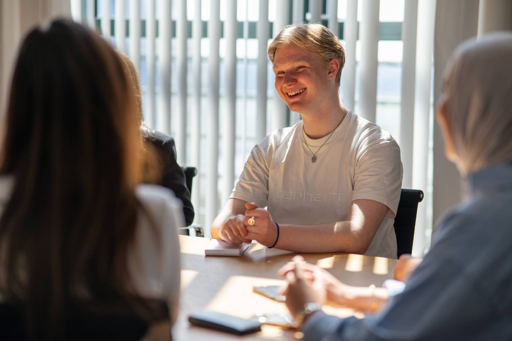 Stagiair Huib lachend op kantoor aan tafel in gesprek met collega's