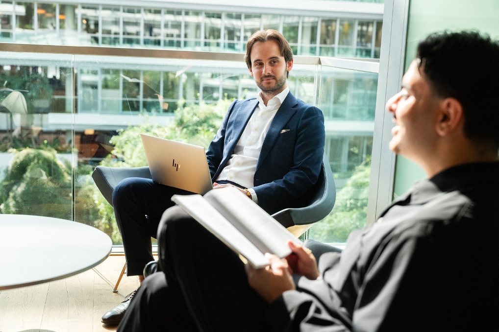 Twee collega's zitten op een stoel in een ruimte en zijn in gesprek