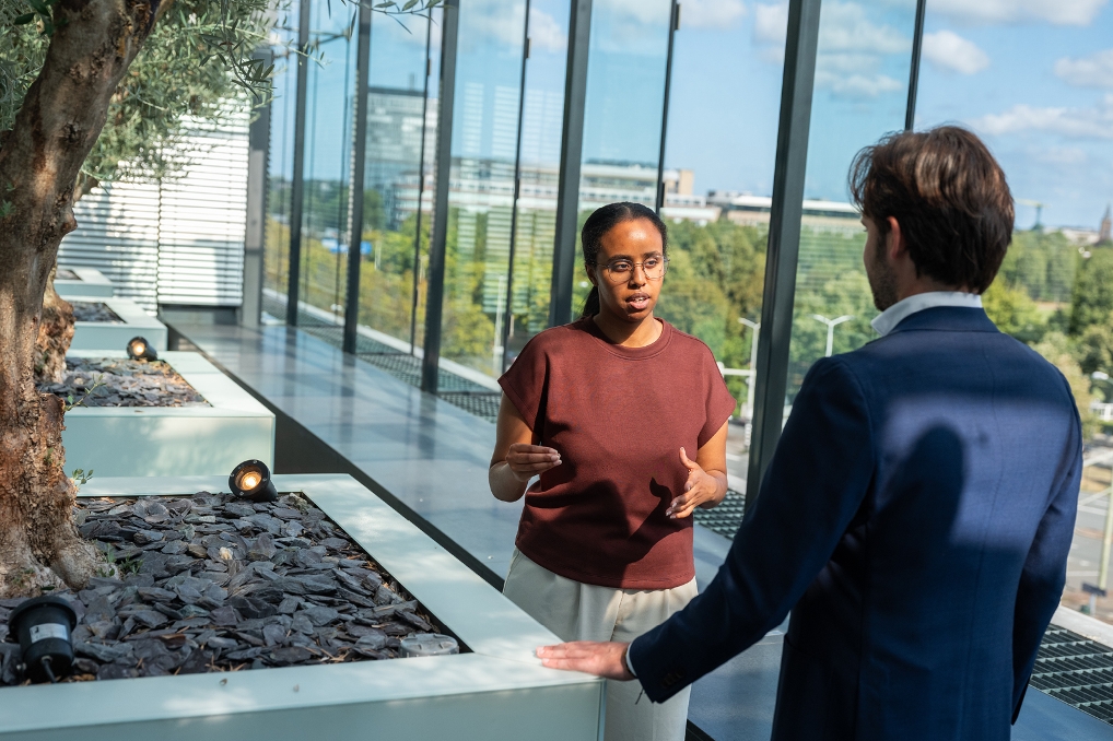Twee collega’s in gesprek op een dakterras bij een kantoorgebouw.