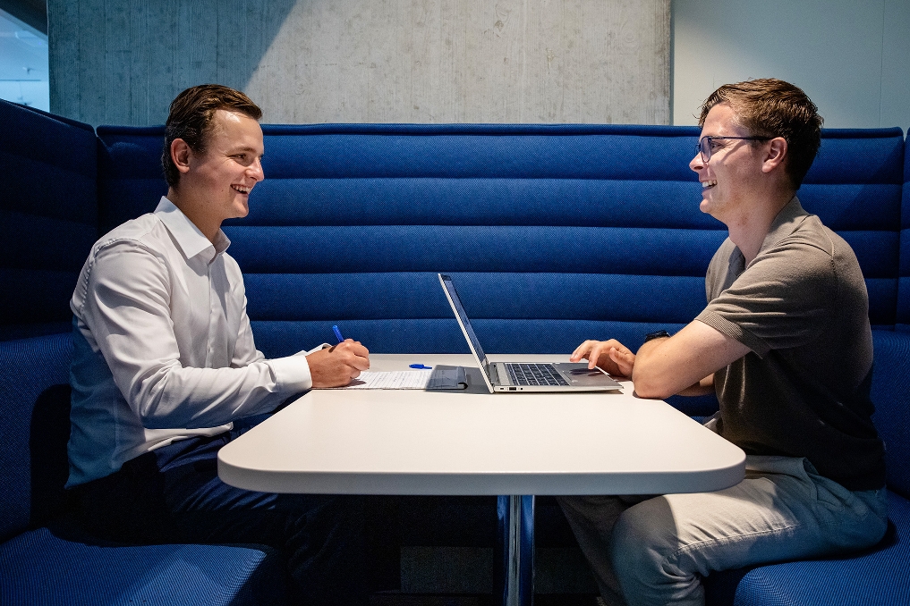 Twee mannen zitten tegenover elkaar aan tafel tijdens een gesprek.