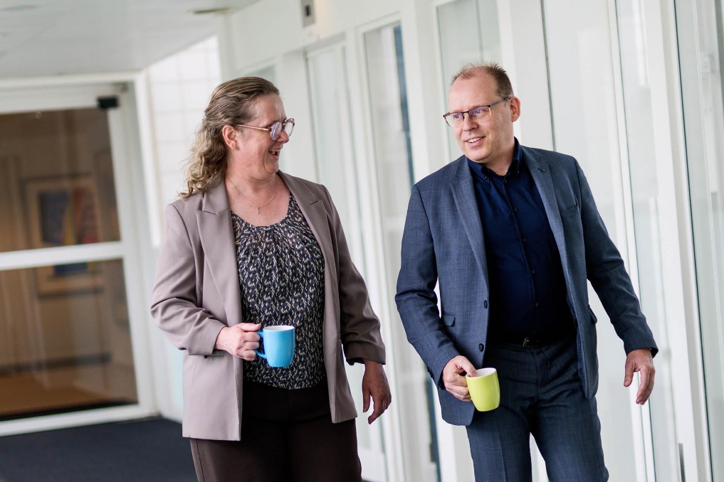 Twee collega’s lopen samen door een kantoor met een mok in de hand.