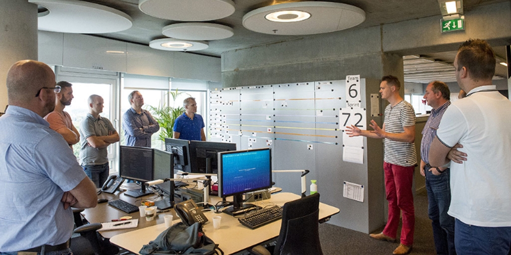 Het team van Jaap op kantoor waar ze staand een sprint meeting houden en een collega zijn tussenresultaten vertelt.
