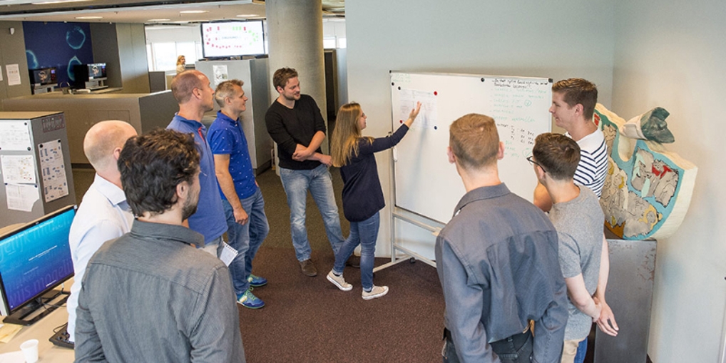 Jaap en zijn team staan voor het whiteboard waar een vrouwelijke collega haar tussenresultaat uitlegt