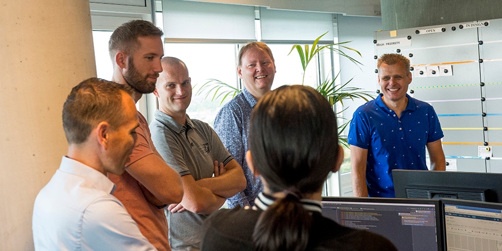 Jaap en een deel van zijn team in een staande meeting, lachend met elkaar