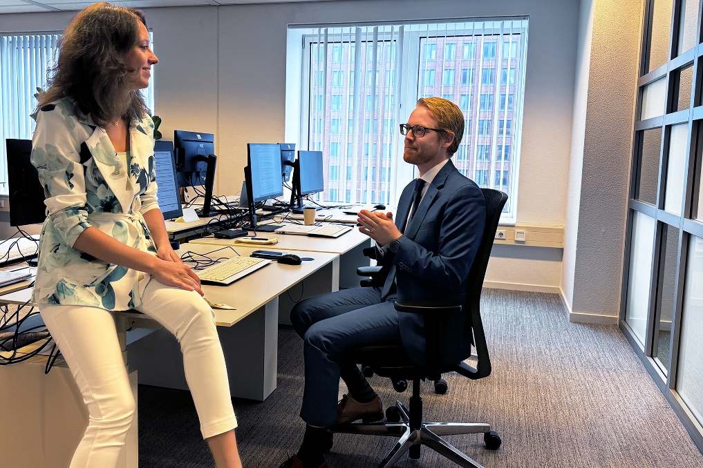 Jean-Paul met een collega in gesprek aan zijn bureau. Hij is jurist bezwaar en beroep bij de Rijksoverheid