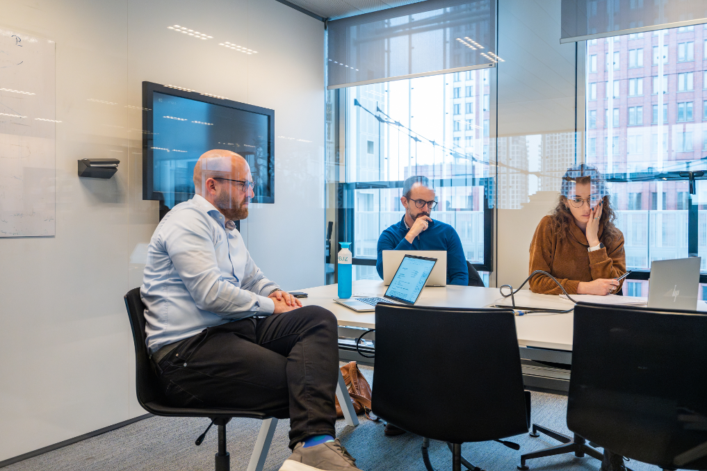 Wilco Ploeg in overleg met collega's in een kamer en op het scherm. Ze zijn juristen bij de Rijksoverheid
